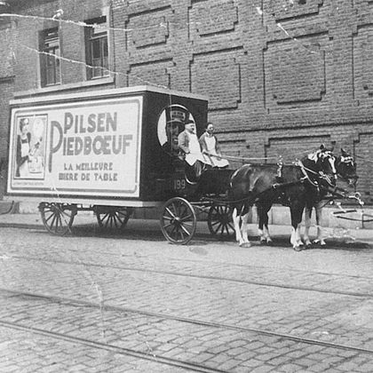 Historic black-and-white photo of a horse-drawn Pilsen Piedbœuf delivery cart, marking Jupiler's founding in 1853.