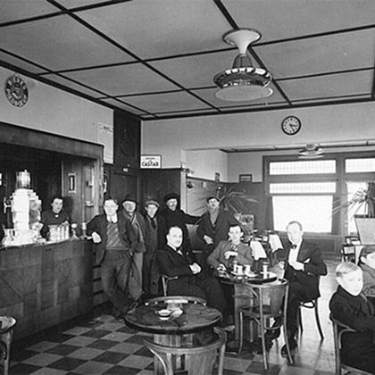 Historic black-and-white photo of men gathered in a Belgian café or pub in 1920, seated at round tables.